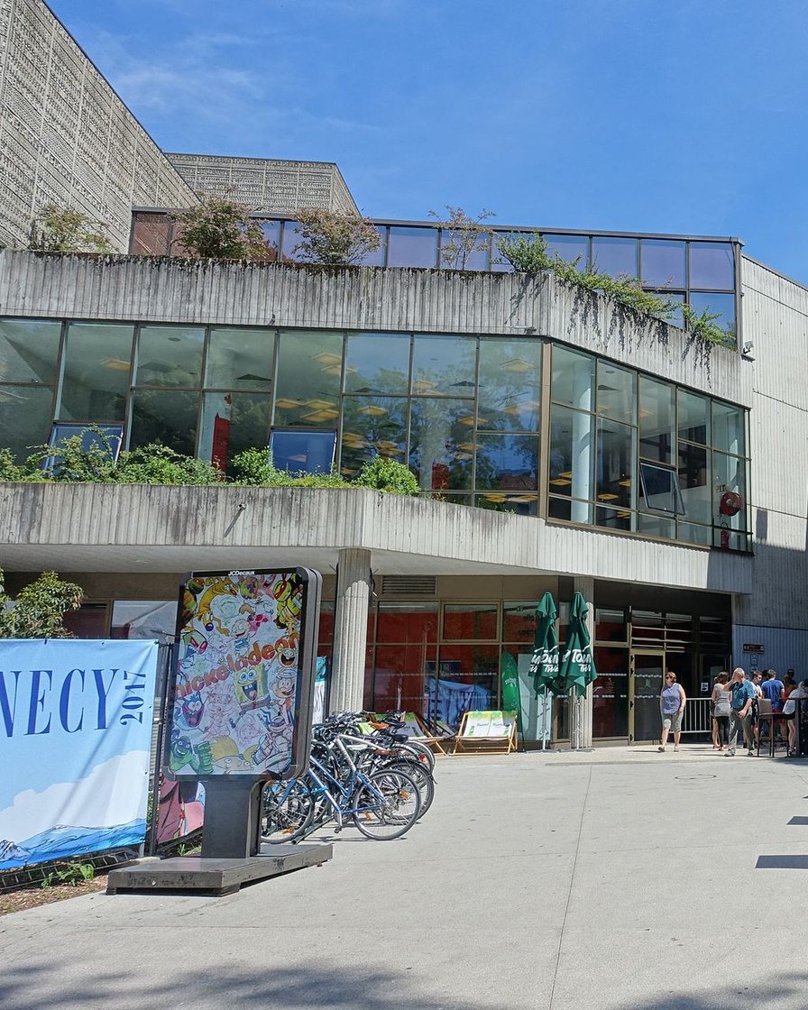 Façade vitrée du centre culturel Bonlieu à Annecy au crépuscule, visiteurs devant l'entrée d'une exposition