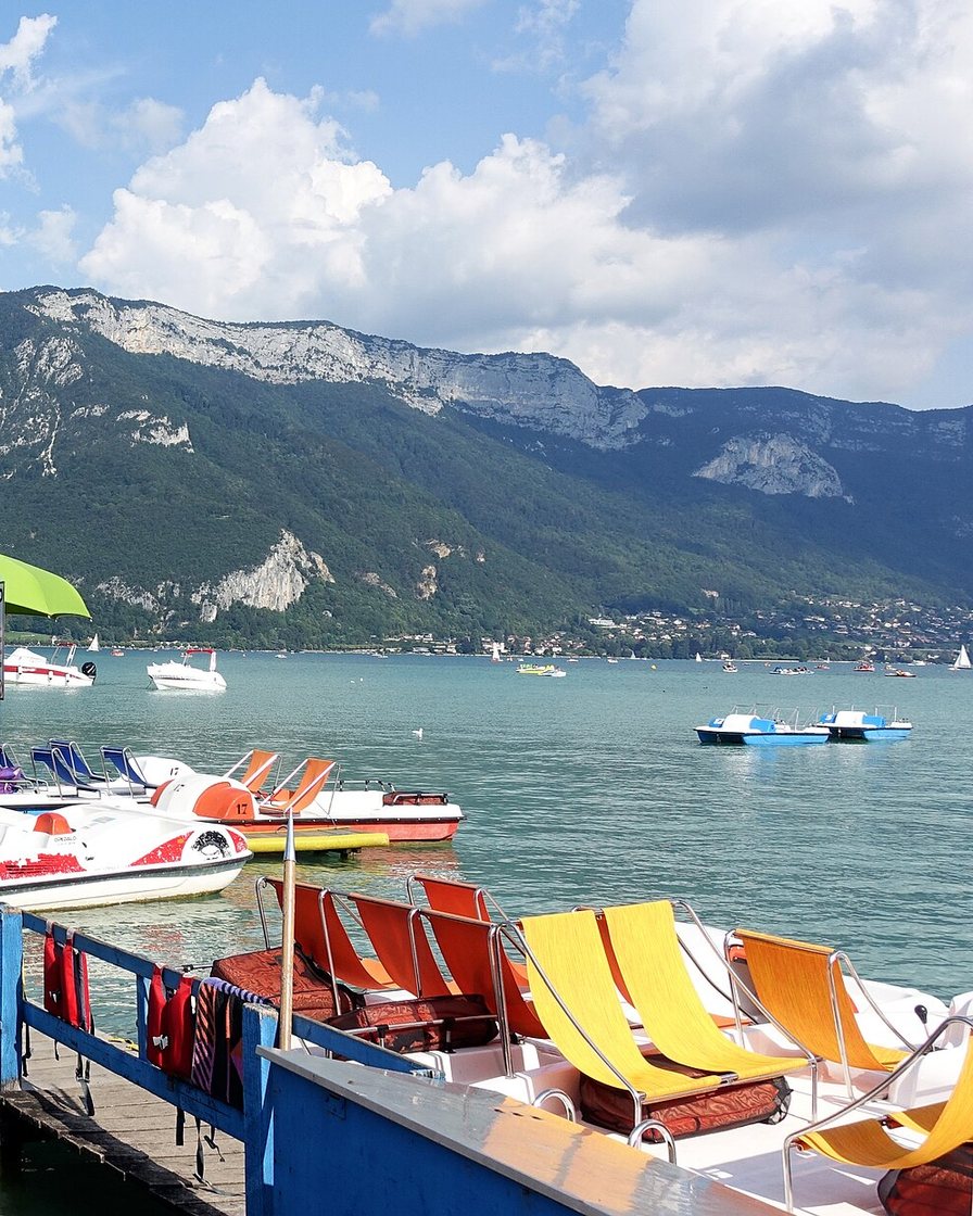 Pédalos et bateaux de location alignés au bord de la pelouse du Pâquier à Annecy par une matinée d'été