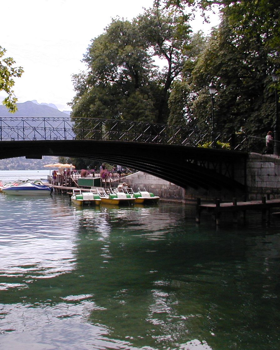 Pont des Amours à Annecy au-dessus du canal du Vassé, bateaux amarrés et eau verte du lac à l'entrée du canal